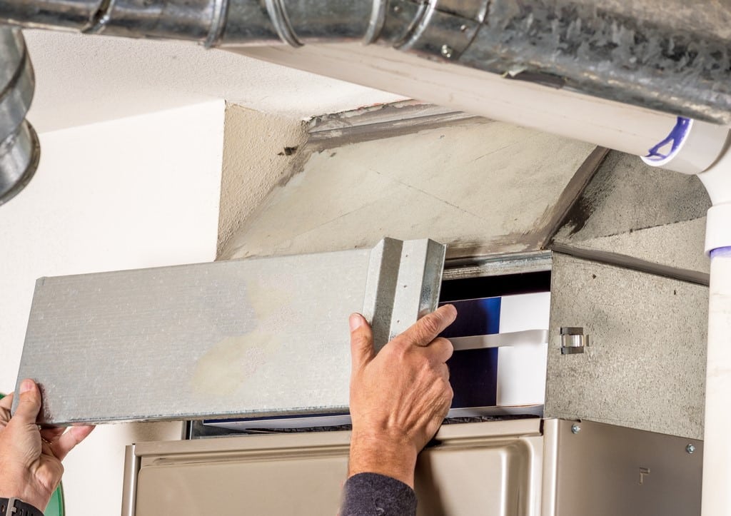 Technician's hands removing the access door on a furnace.