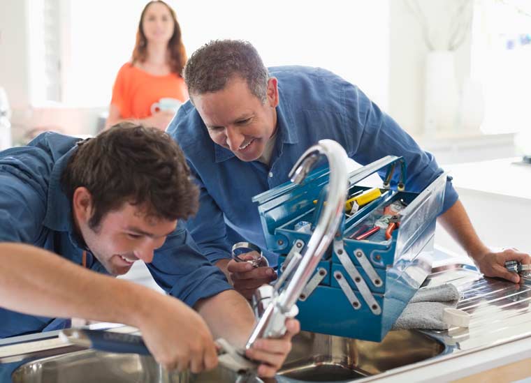 Two plumbers working beside kitchen sink.